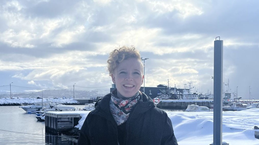 Bilde av inspektør Anne Orheim, smilende  foran ei småbåthavn, med en fabrikkbygning i bakgrunnen