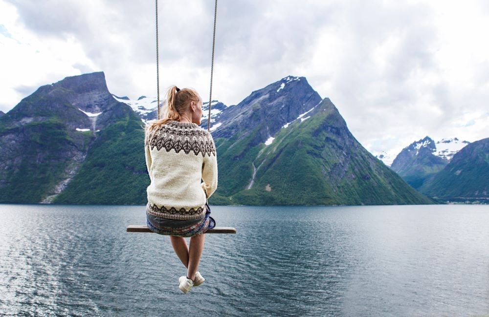 Bildet viser ei kvinne som sitter på ei huske foran en fjord. 