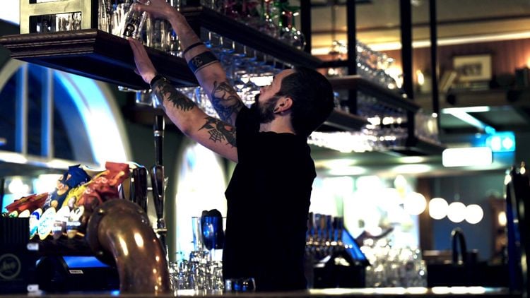 Bartender henter ned glass bak en bar.