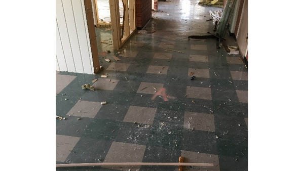 Bildet viser en korridor i et bygg som holder på å bli revet. Noen veggplater er allerede fjernet. Gulvet er laget av noe som ser ut som linoleumsfliser, men som er asbestholdige vinylfliser. Gulvet er merket med en A for Asbest