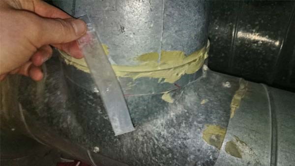 Bildet viser nærbilde av en skjøt i en ventilasjonskanal av metall. En gul fugemasse er brukt som tetning i skjøten.