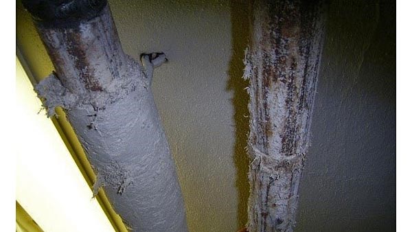 Bildet viser nærbilde at to metallrør som henger i et tak. Det ene røret har rørisolasjon av en fibermasse som inneholder asbest. Det andre røret er delvis sanert og har bare rester av isolasjonen igjen.