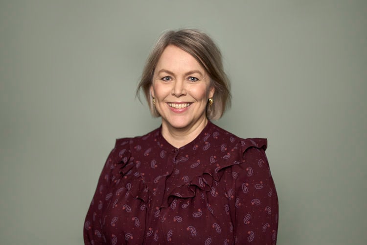 Kvinne med blondt hår og vinrød skjorte smiler til kamera.