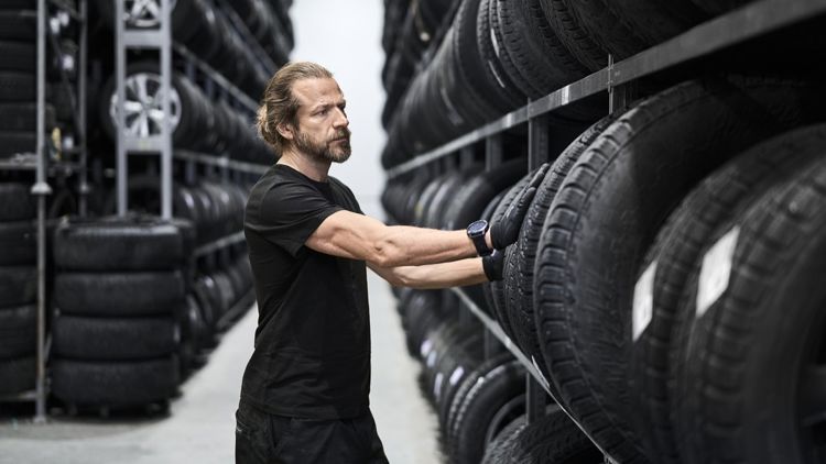 Mann står mellom reoler med bildekk og tar ut et dekk.