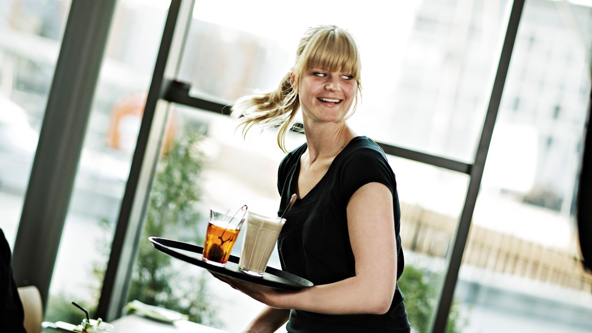 Kvinnelig servitør bærer et serveringsbrett med drikke.