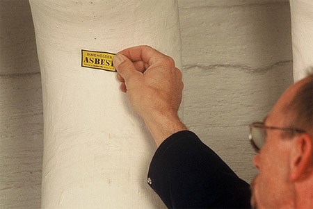 Bildet viser en mann som merker et rør med et klistremerke som det står asbest på.