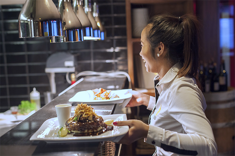 Bildet viser en servitør som henter mat fra kjøkkenet på en restaurant.