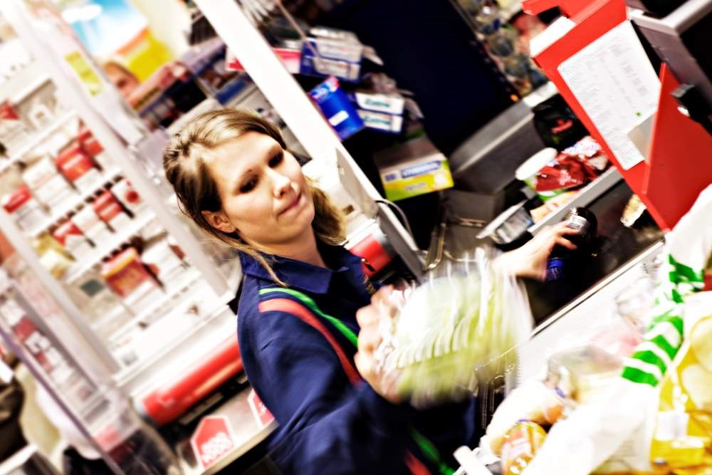 Ung kvinnelig butikkmedarbeider som jobber i kassa på en dagligvarebutikk