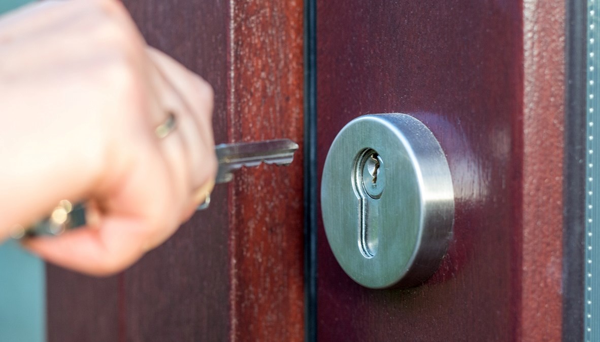 Bildet viser ei hånd som stikker en nøkkel inn i et nøkkelhull på ei dør. 