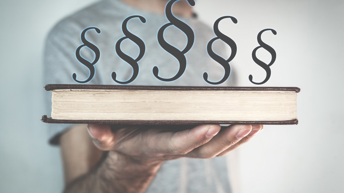 Bildet viser en mann som holder ei bok i håndflaten. Over boken er det redigert inn fem lovparagraftegn.