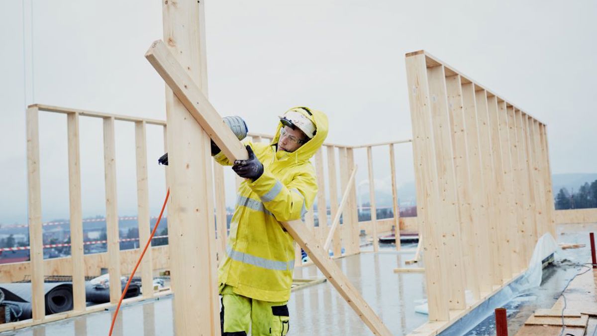 Bildet viser en arbeider som jobber på toppen av et tak. Han holder treverk. 