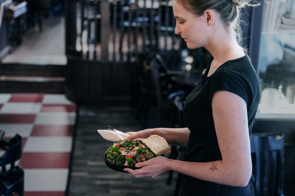 Bildet viser en kvinnelig servitør som holder i en tallerken med mat. 