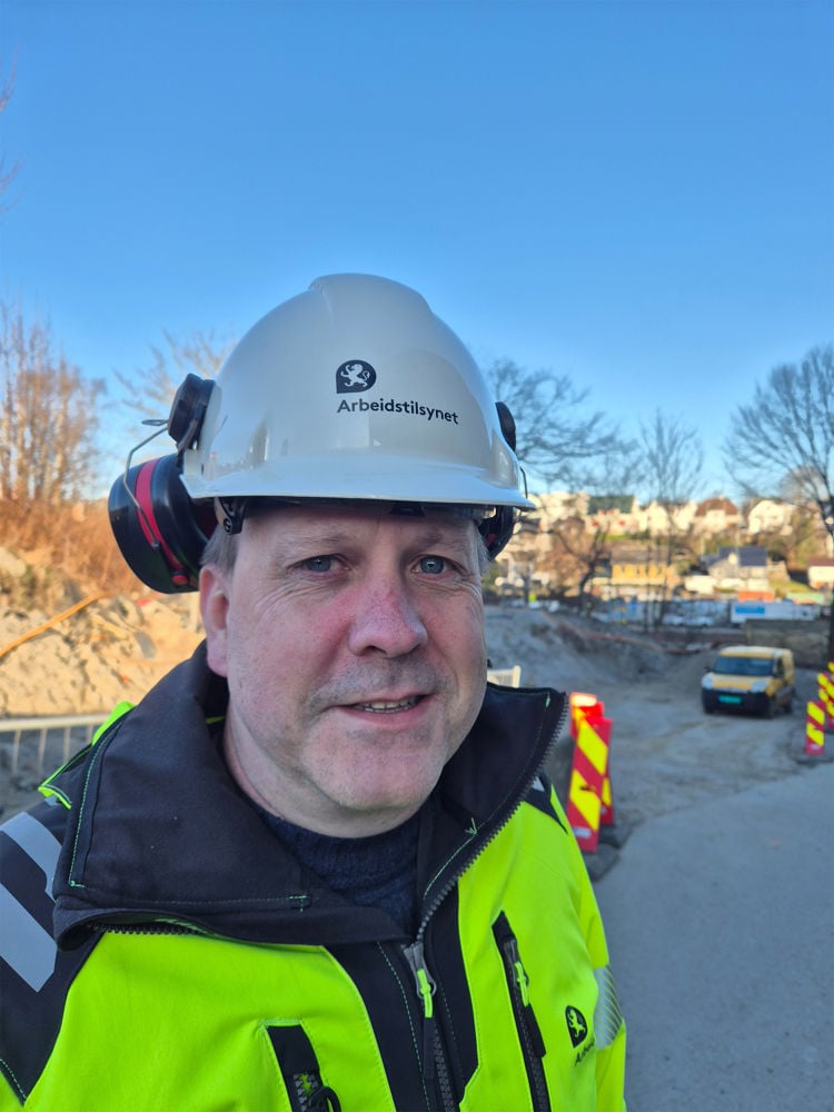 Mann i arbeidsklær og hjelm ser i  kamera 