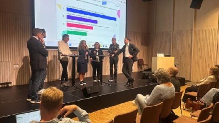 Seks personer står på en scene under en paneldebatt 