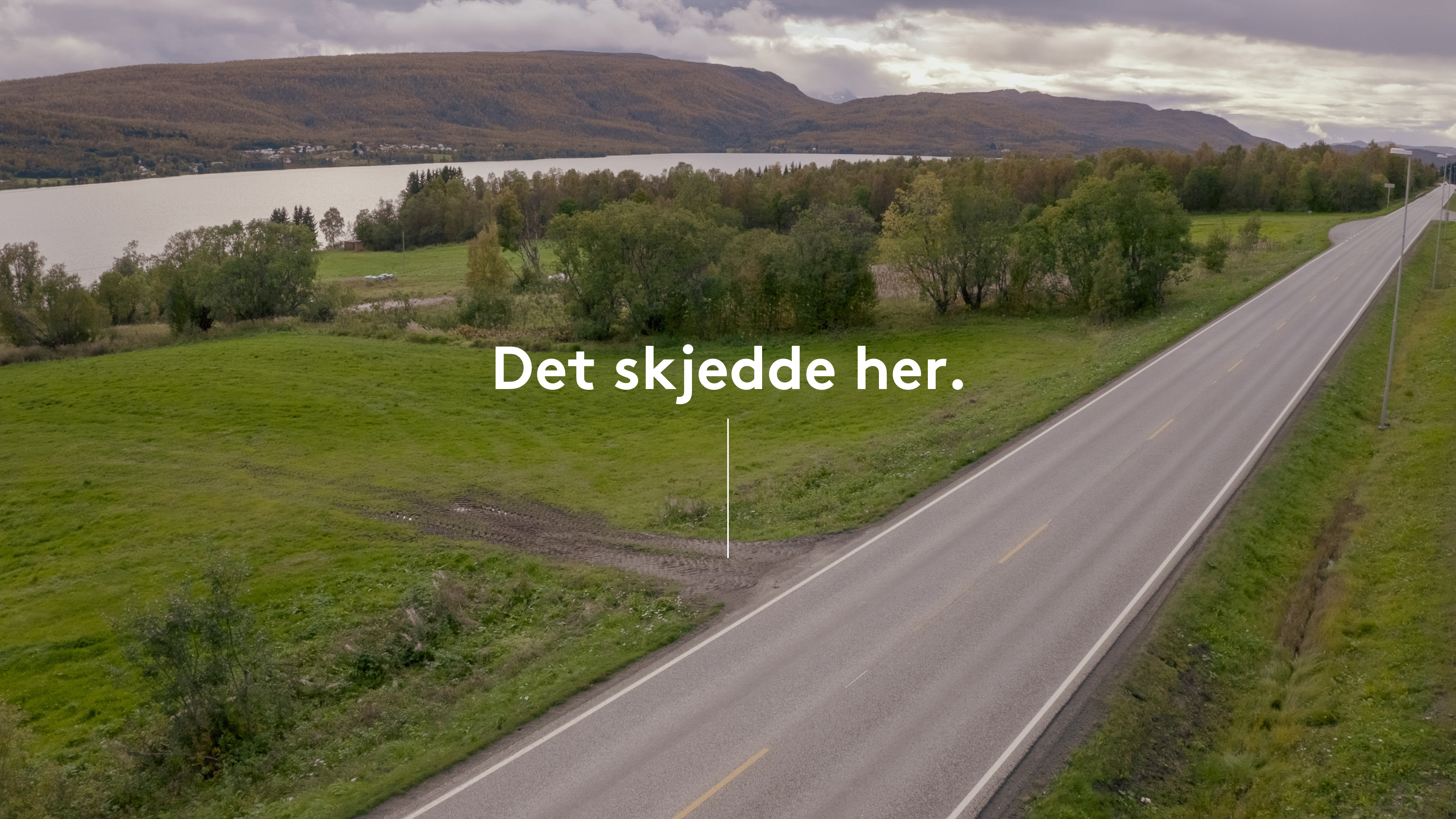 Oversiktbilde med en vei og grønne markre rundt, som har teksten "Det skjedde her" skrever over. Foto.